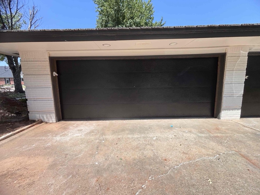 Black modern garage door installed on white brick home