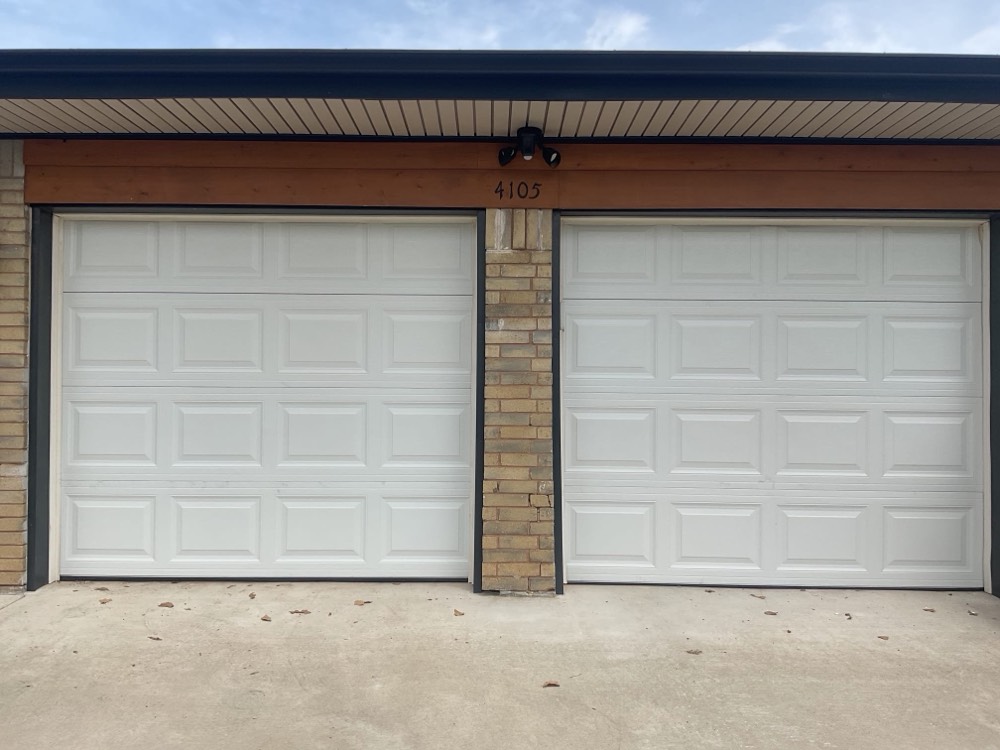 Two white garage doors on brick residence with overhead trim.