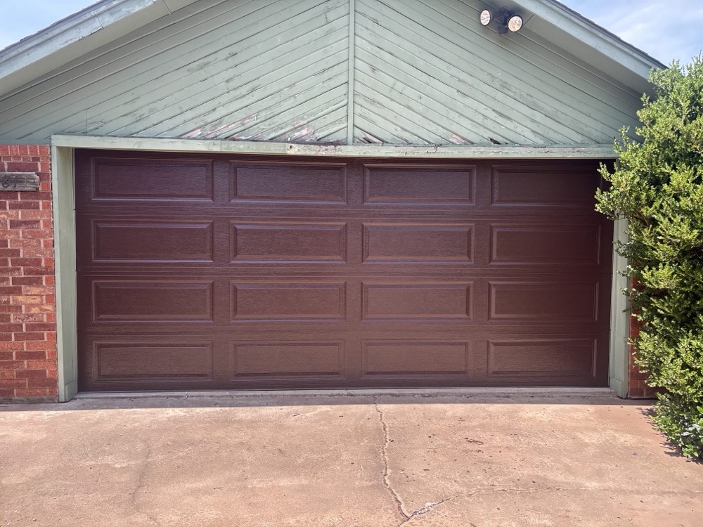 New burgundy garage door installed on brick home with concrete driveway