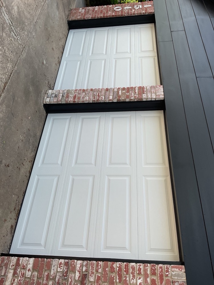 Two white nine-panel garage doors installed in brick garage opening