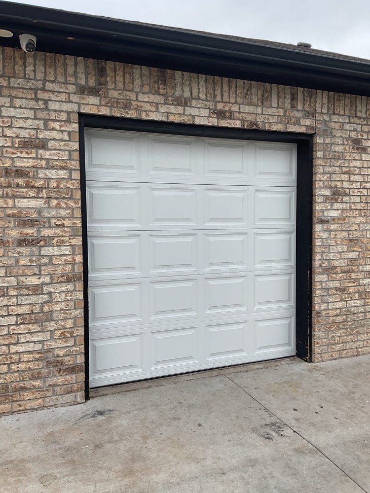 White six-panel garage door installed on brick home in Norman
