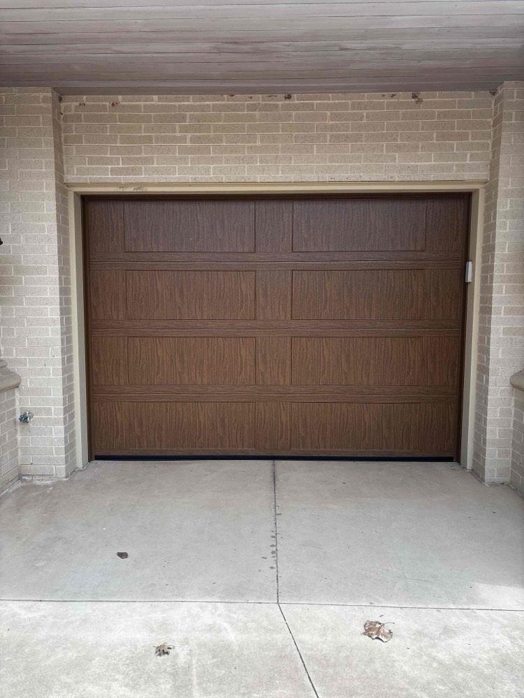Brown wood-grain garage door installed on brick home
