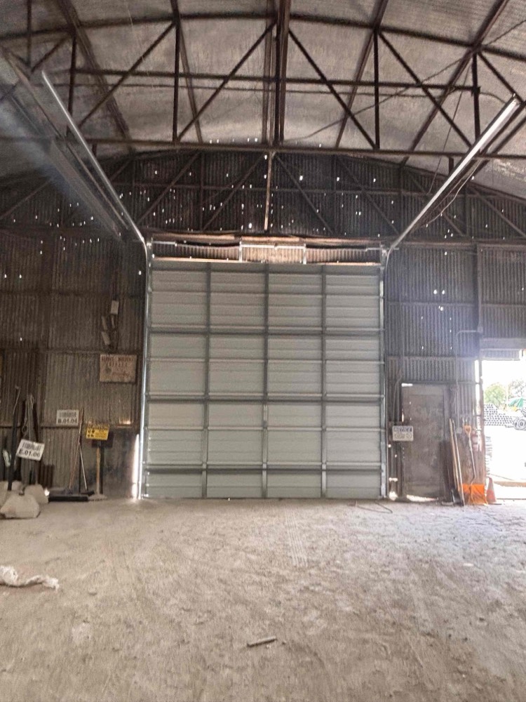 Newly installed light gray sectional garage door in industrial building with metal framework.