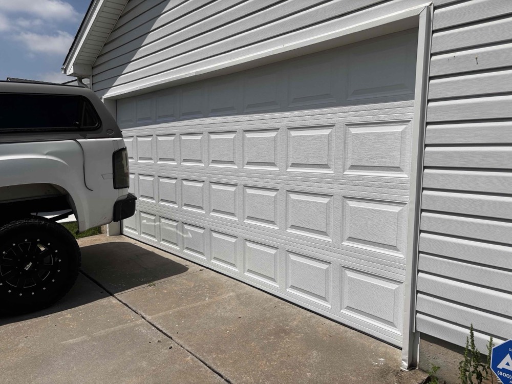 White garage door installation with open position revealing interior frame and driveway
