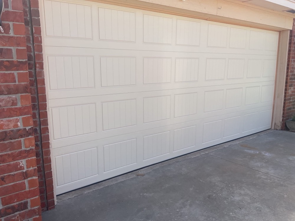Completed white garage door installation with visible panel sections and concrete driveway.