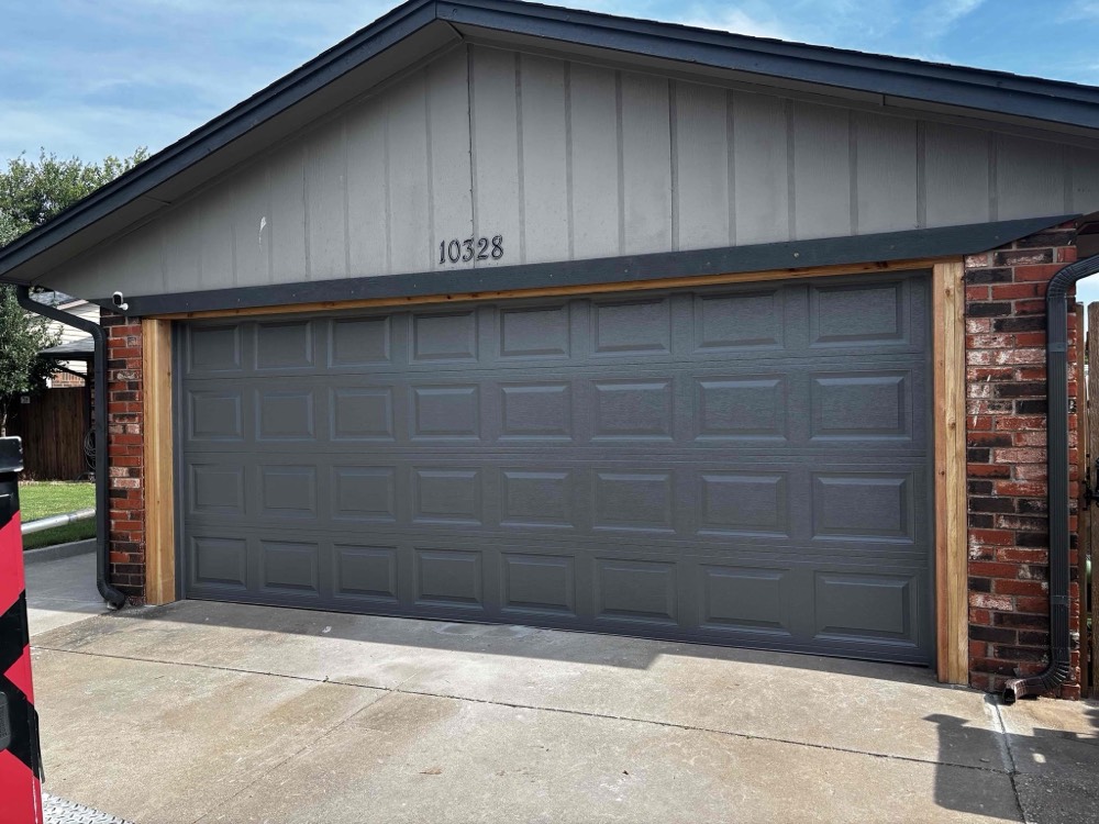 Installed gray garage door with wood-trimmed frame and brick exterior