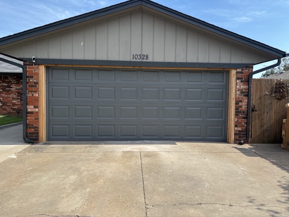 Gray raised-panel garage door with wood trim on brick garage in Yukon, OK