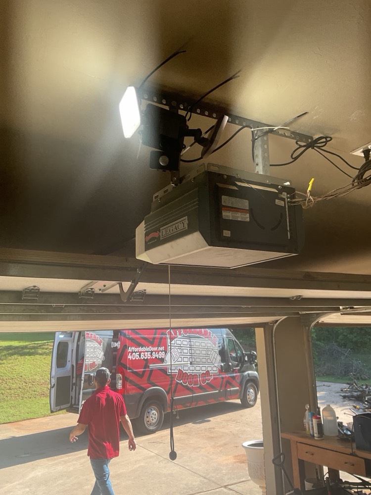 Professional garage door opener installation with bright LED lighting fixture mounted overhead.