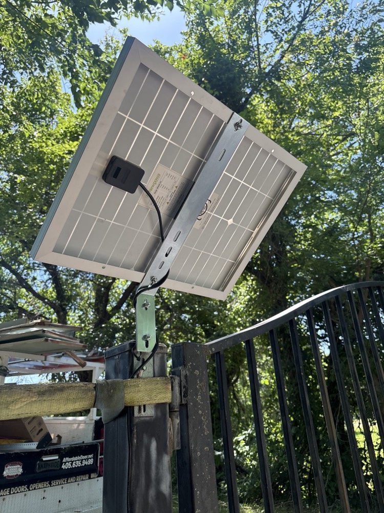 Solar-powered gate opener mounted on wooden support post with wiring.