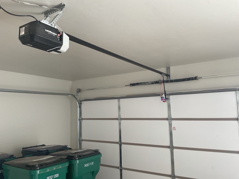 Installed garage door opener motor mounted on garage ceiling with black rail and hardware.