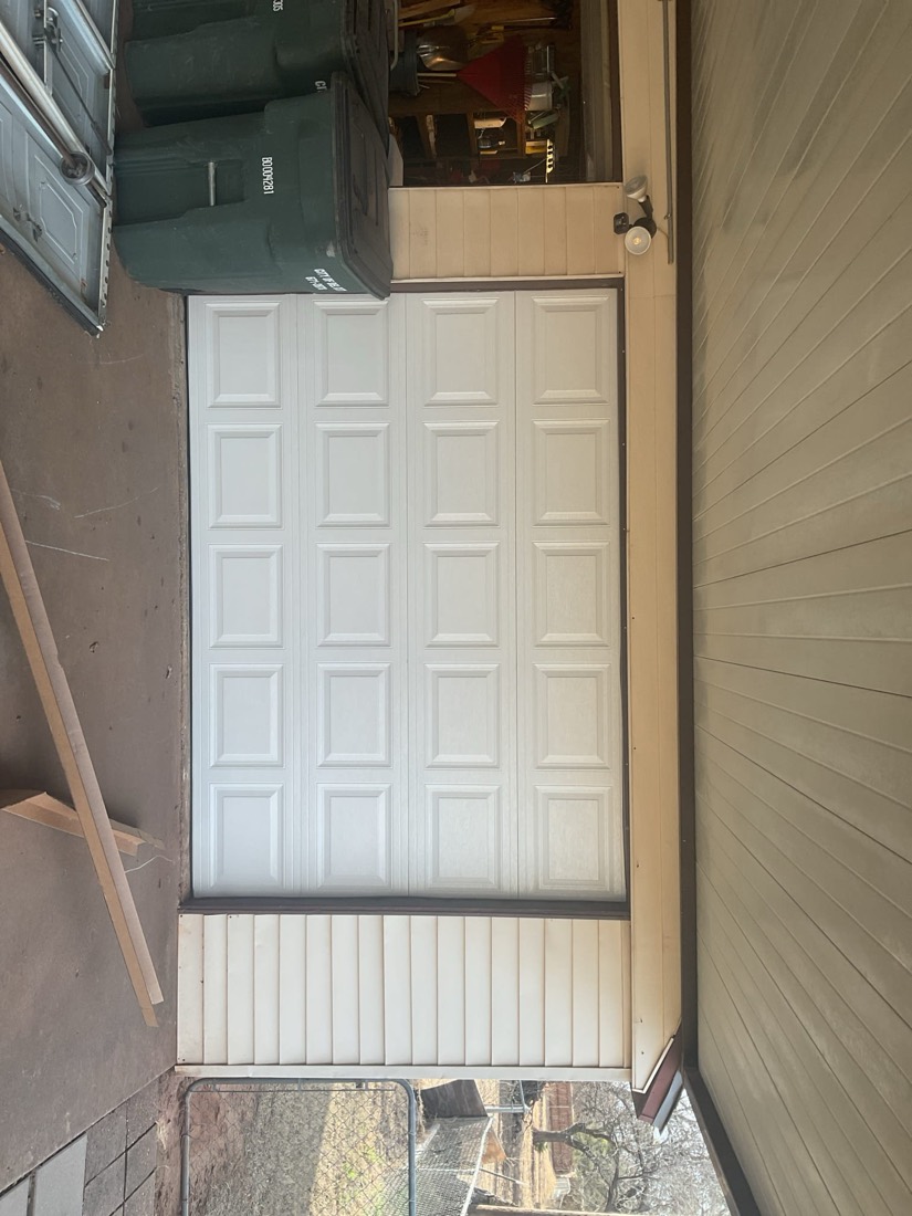 Installed white panel garage door in garage opening with frame visible.