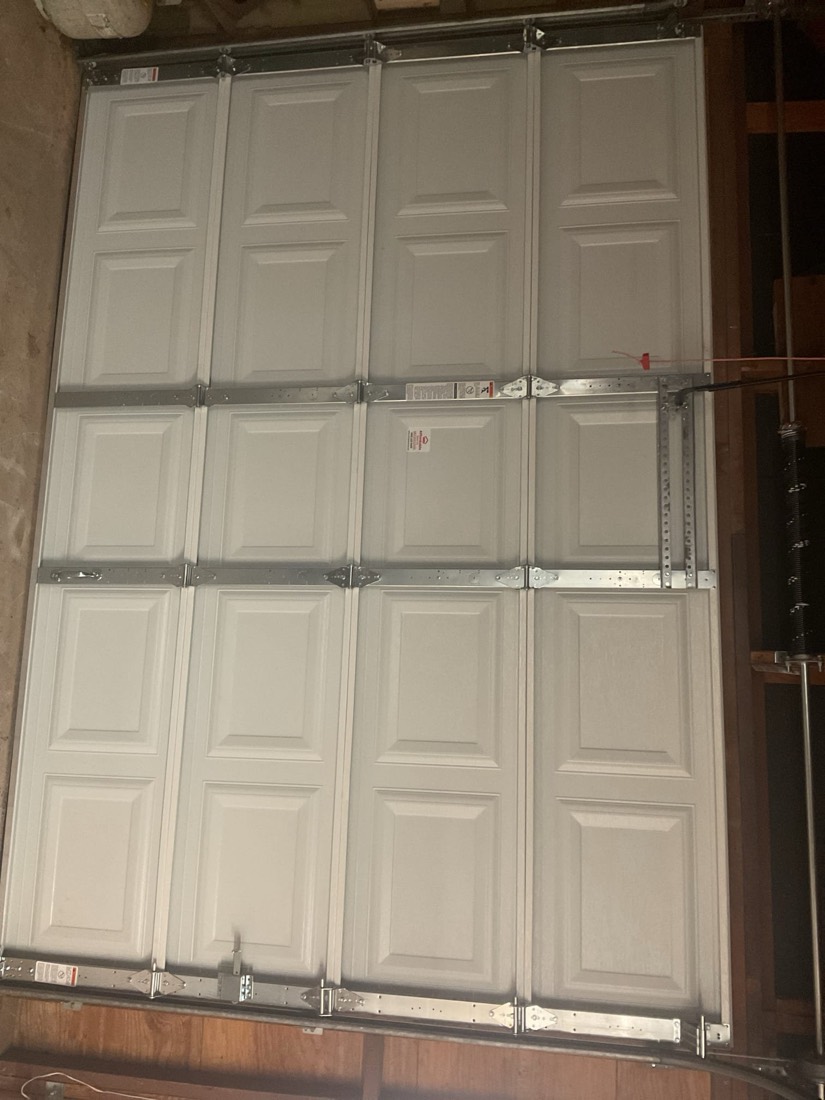 White multi-panel garage door with horizontal tracks and hardware installed.