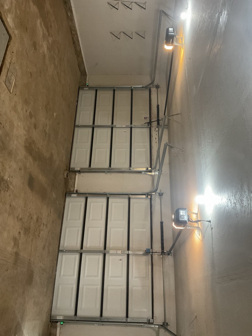 Newly installed white garage door with professional hardware and lighting.