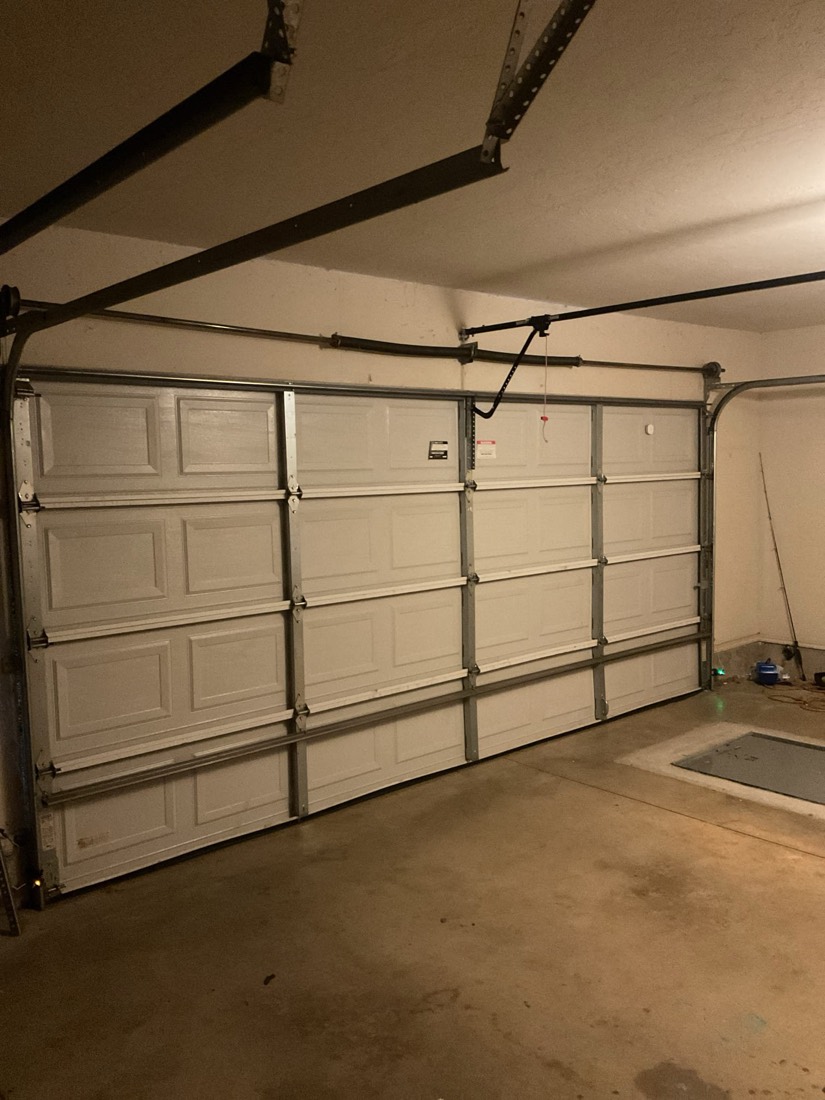 White paneled garage door with installed opener and tracks in garage interior