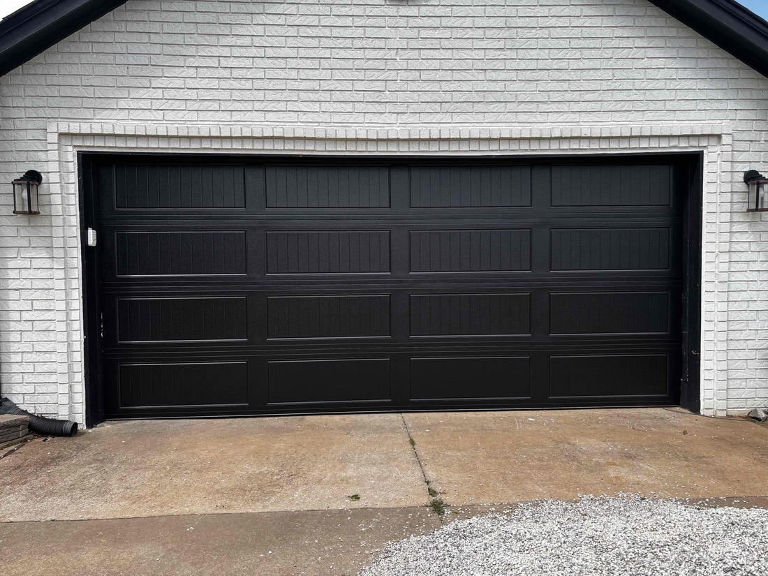 Black paneled garage door installed on white brick home
