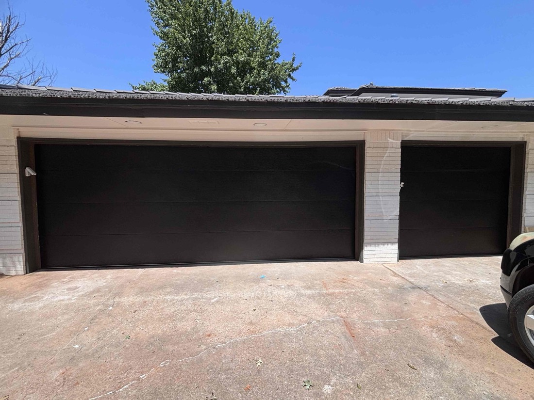 Two black garage doors installed on white brick home exterior