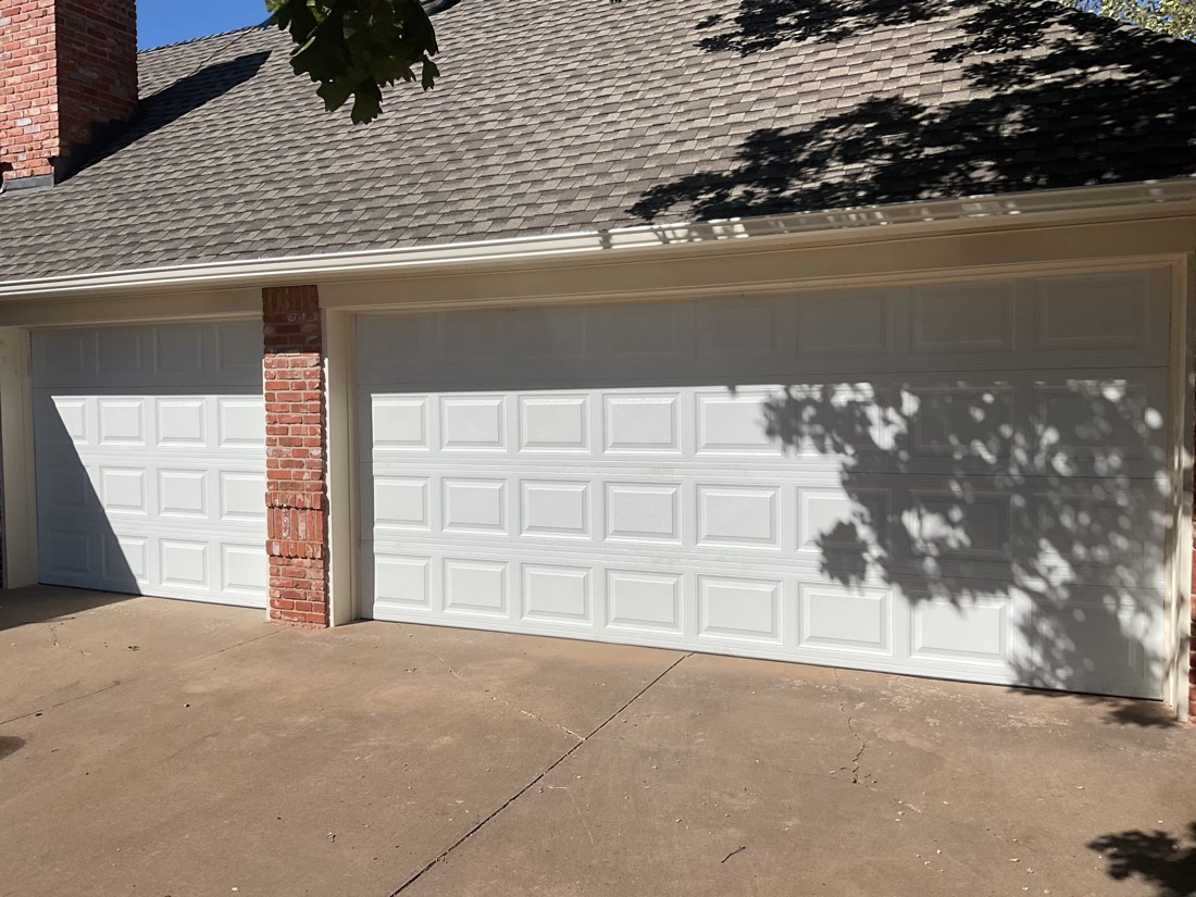 Two white panel garage doors on a brick home with driveway