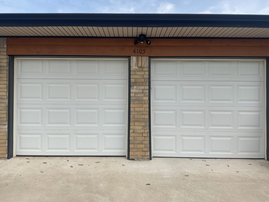 Two white garage doors on brick residence with overhead trim.