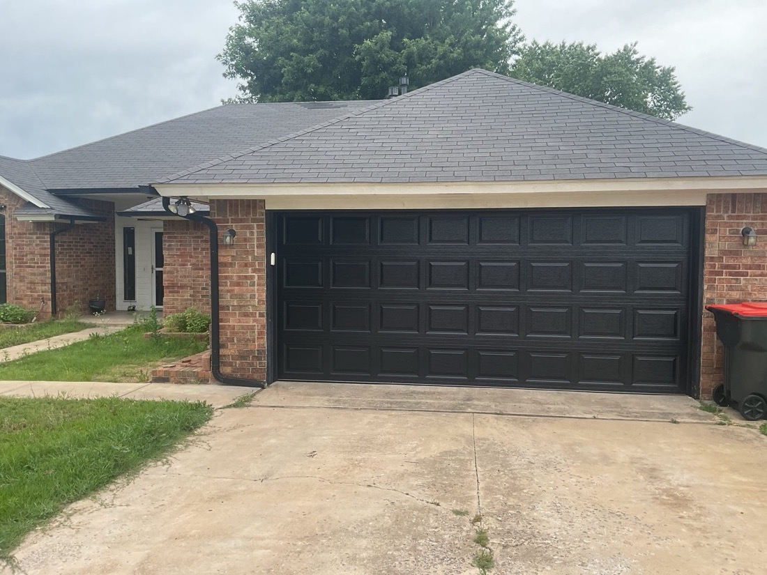 Black multi-panel garage door installed on brick home exterior
