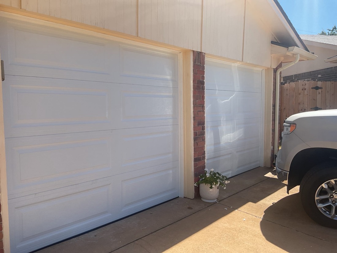 Two white installed garage doors on a residential driveway in daylight