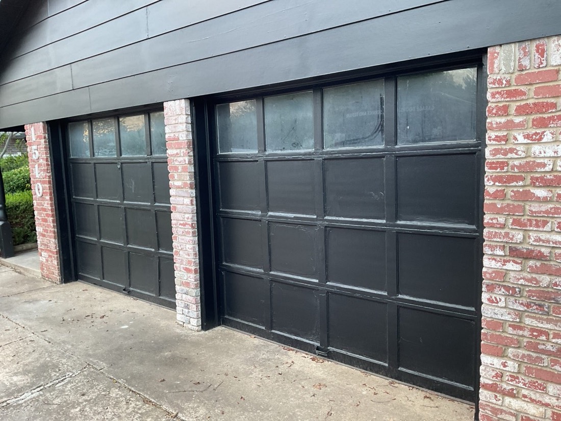 Two black multi-panel garage doors with glass window inserts