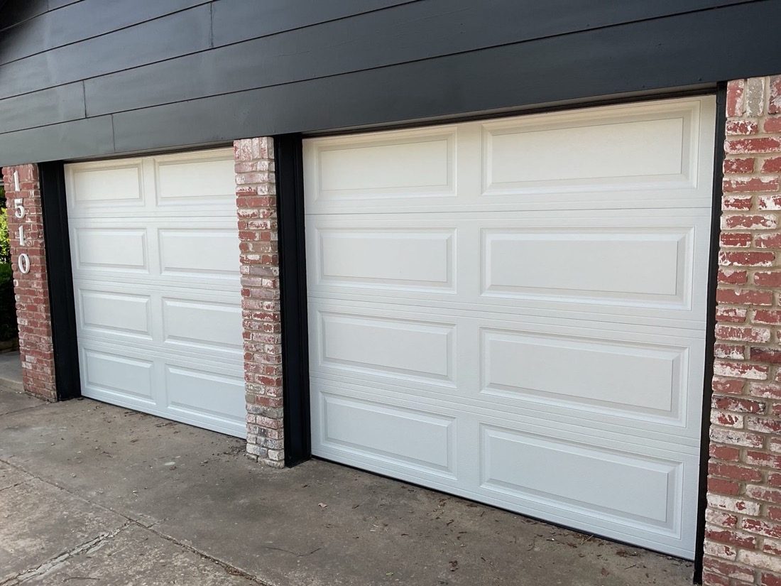 Two white nine-panel garage doors installed in brick garage opening