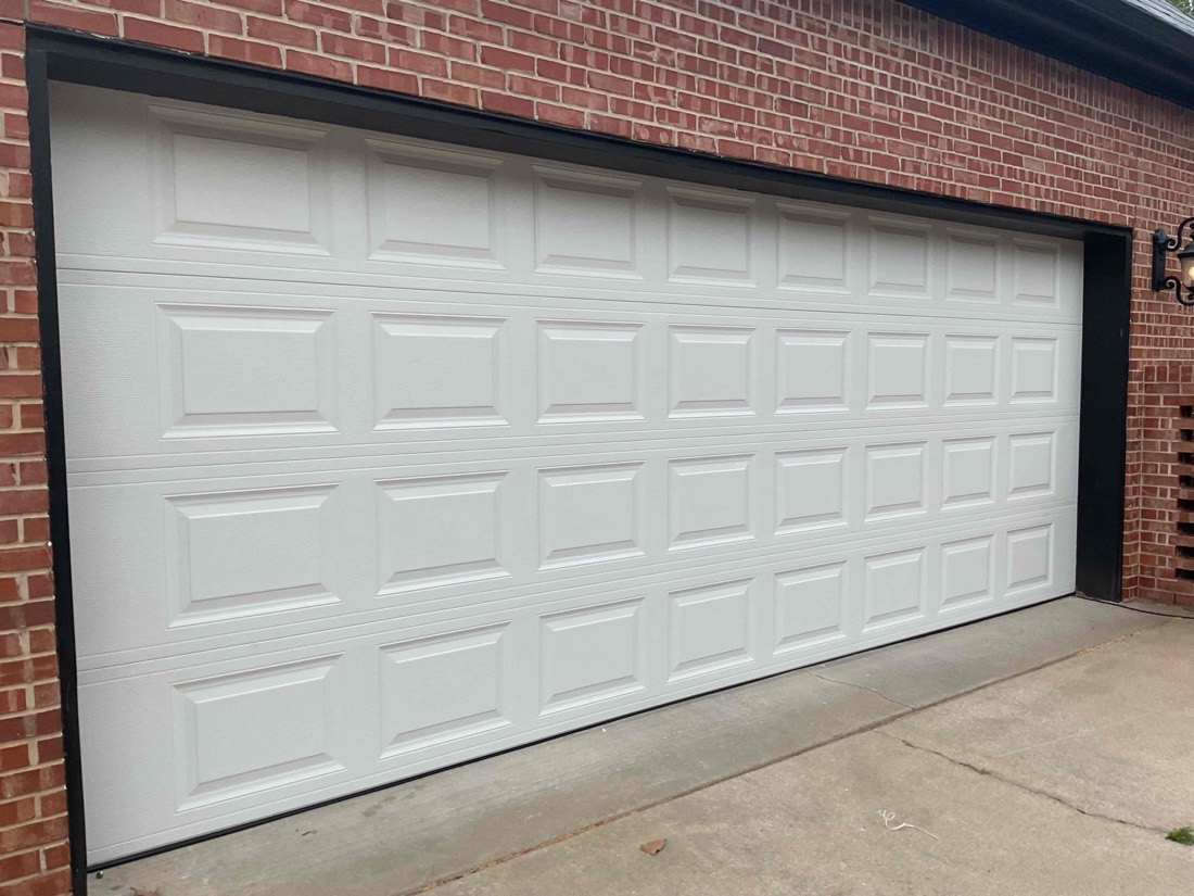 White raised-panel garage door installed on brick exterior with black trim