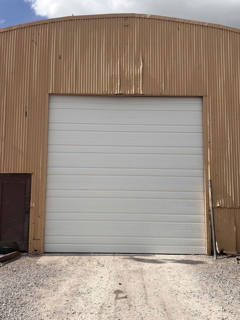 White sectional garage door installed on tan corrugated metal commercial building exterior.