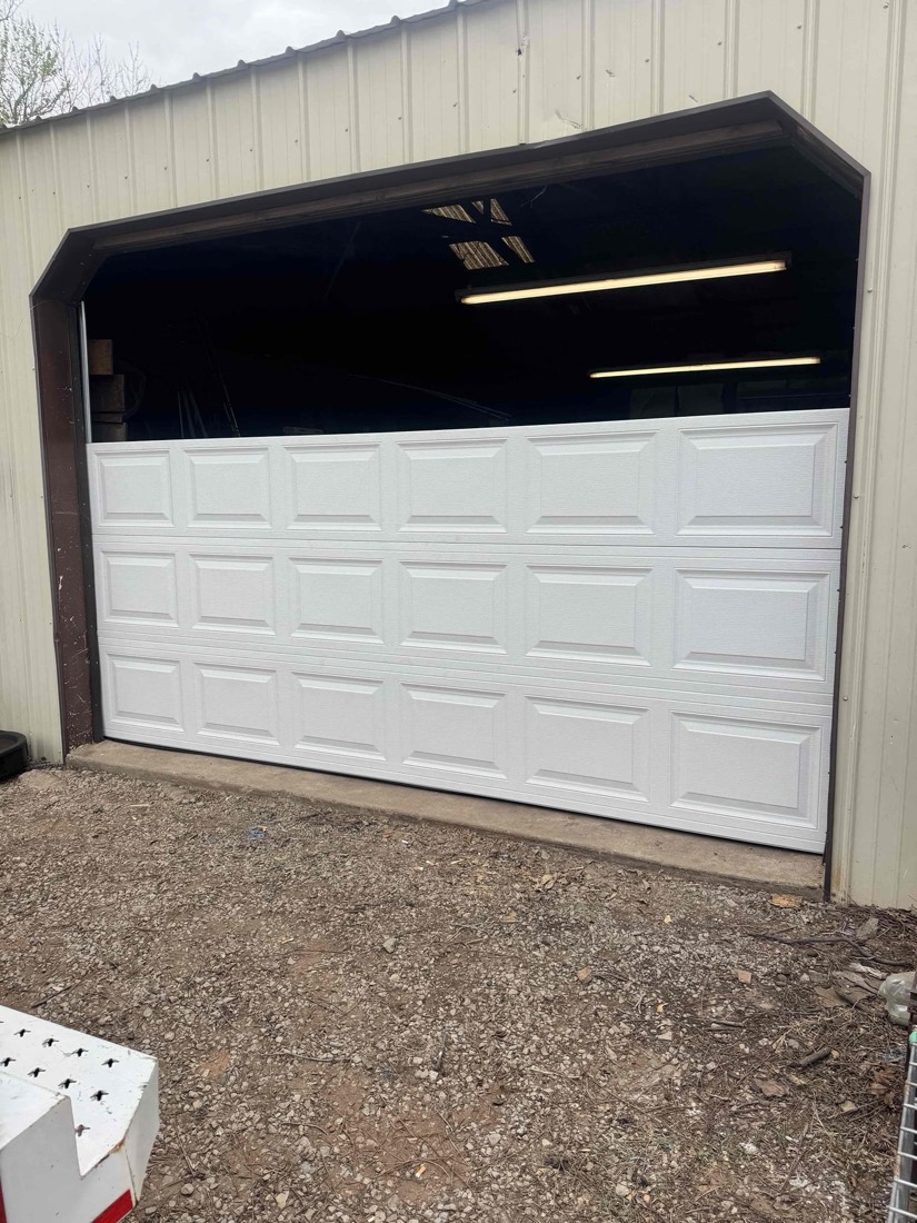 Newly installed white raised-panel garage door in metal building.