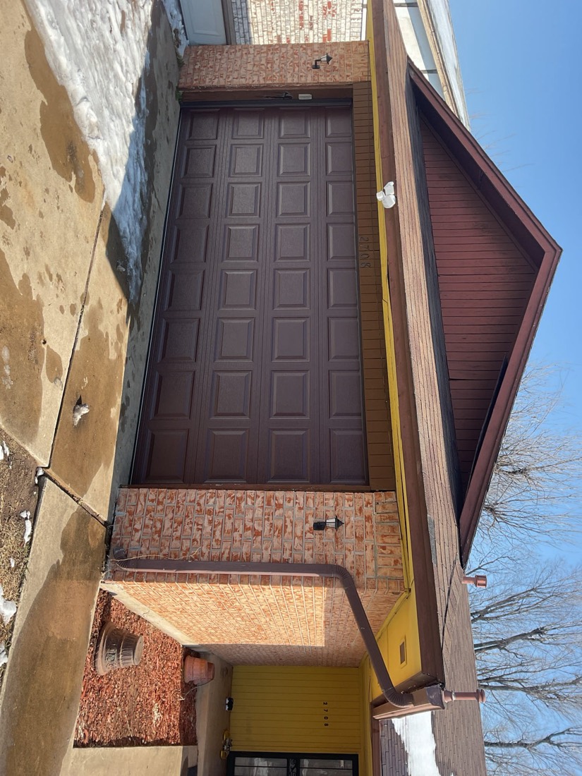 Newly installed dark brown garage door on brick house with yellow trim in Spencer, OK.