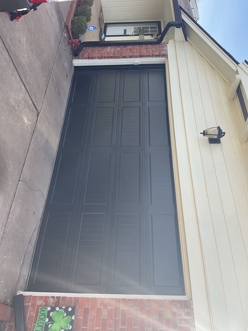 Black residential garage door with raised panel design on brick garage.