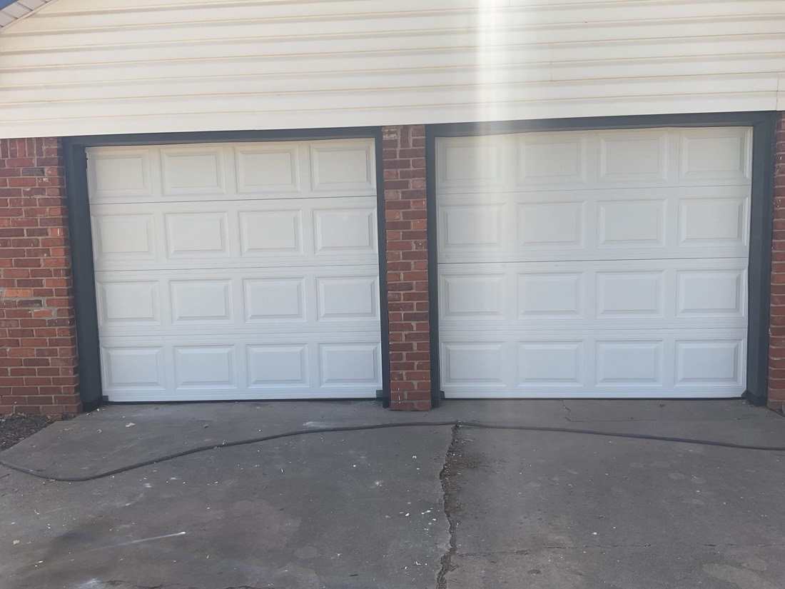 Two white panel garage doors mounted on a brick home exterior.