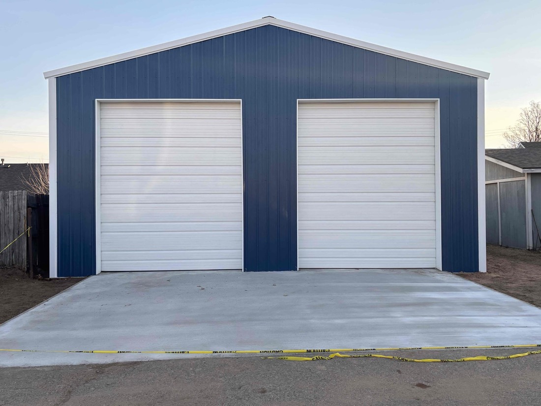 Two white garage doors on blue metal building with concrete driveway