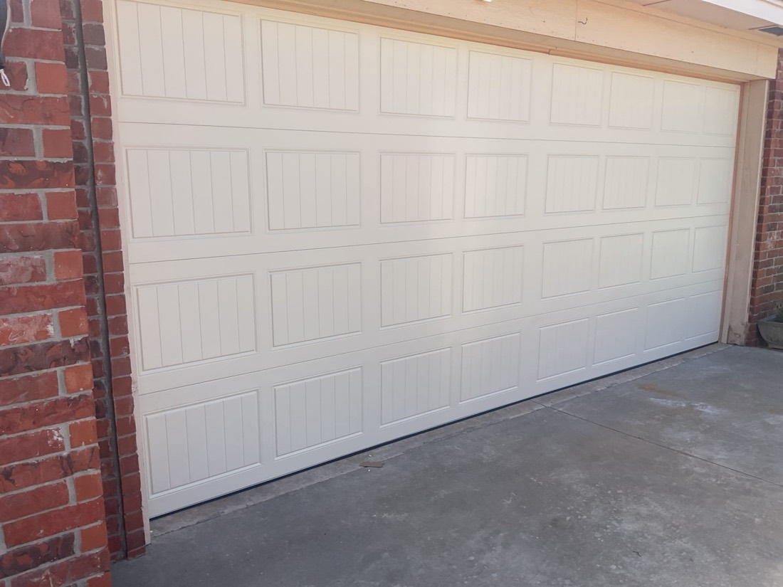 Completed white garage door installation with visible panel sections and concrete driveway.