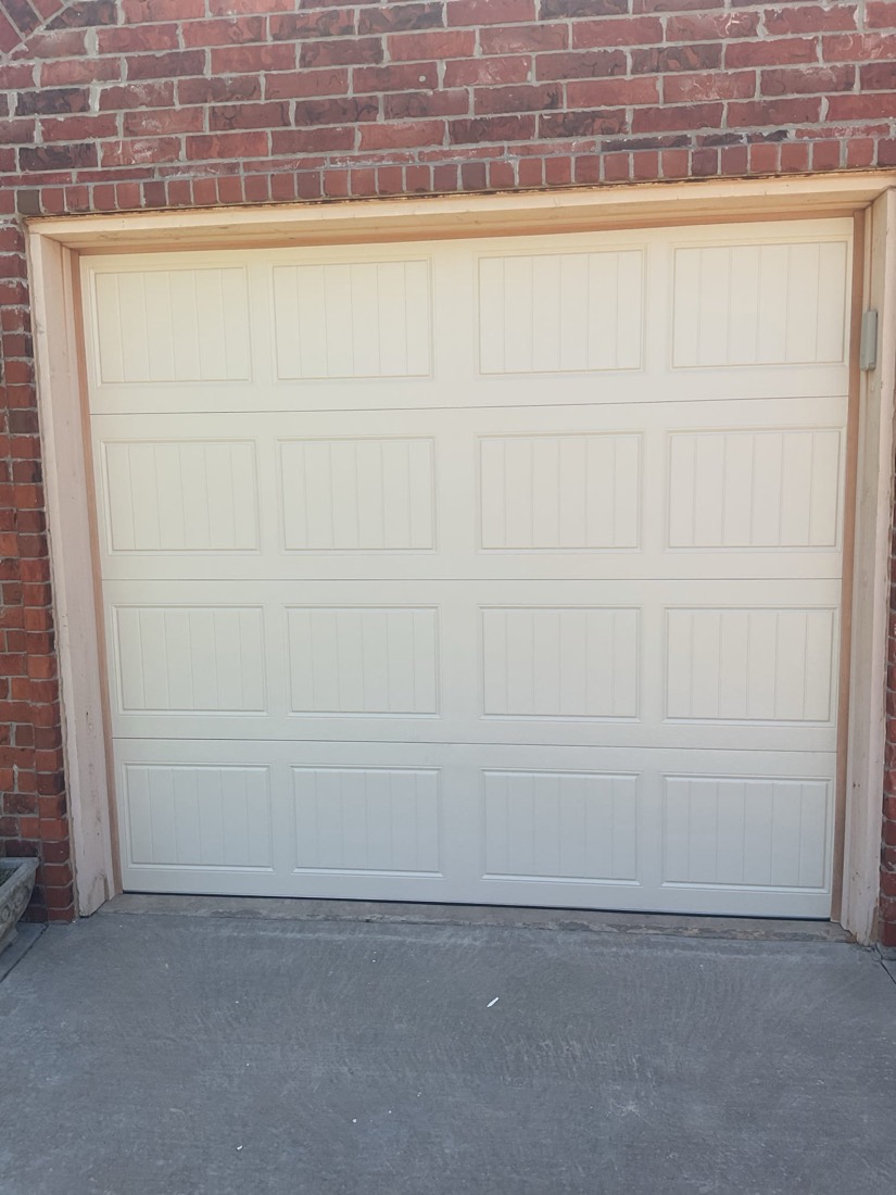 Newly installed white garage door with raised panel design on brick exterior.