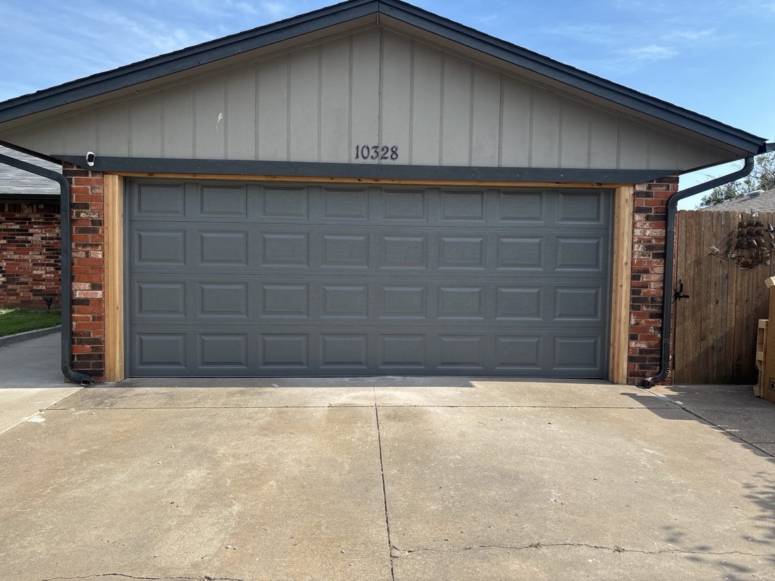 Gray raised-panel garage door with wood trim on brick garage in Yukon, OK