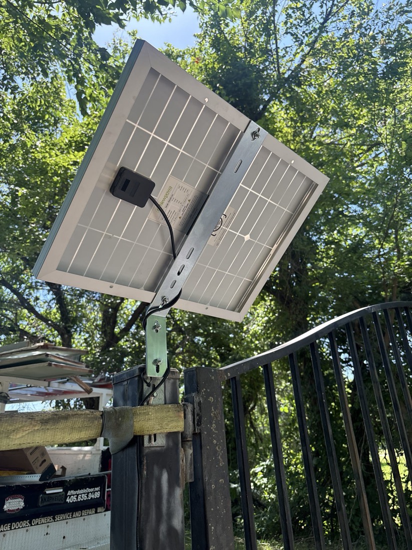 Solar-powered gate opener mounted on wooden support post with wiring.