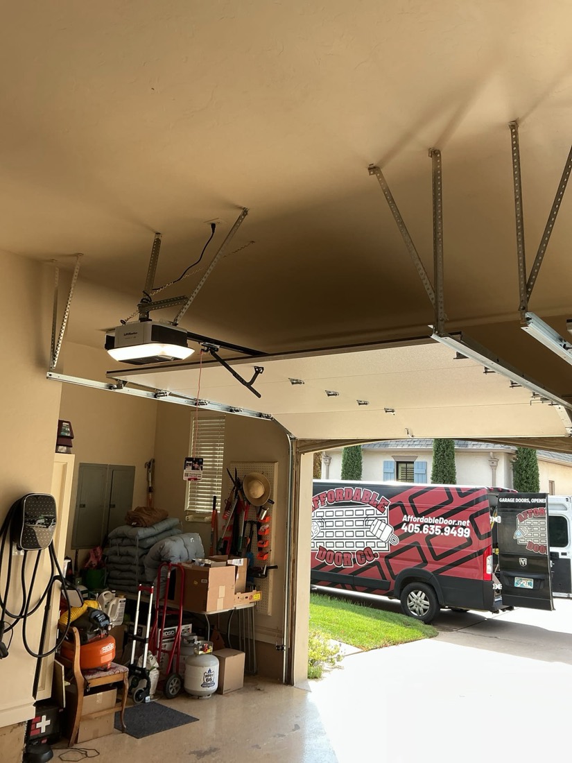 Newly installed garage door opener motor with support brackets and cables on garage ceiling.