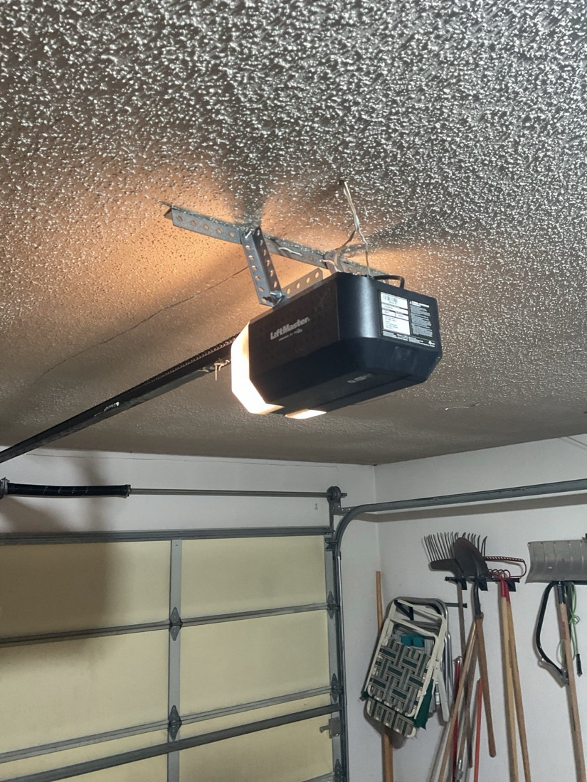 Black garage door opener motor mounted to textured garage ceiling.