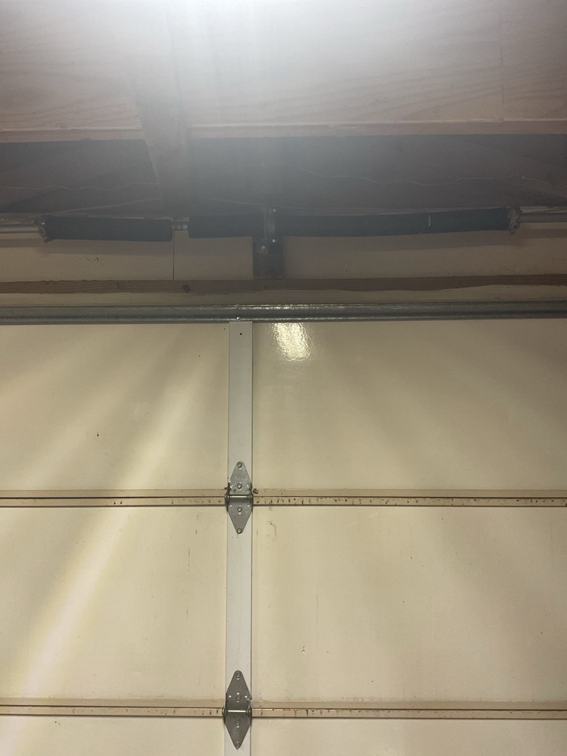 Newly installed garage door spring and hardware visible on cream-colored residential garage door panels