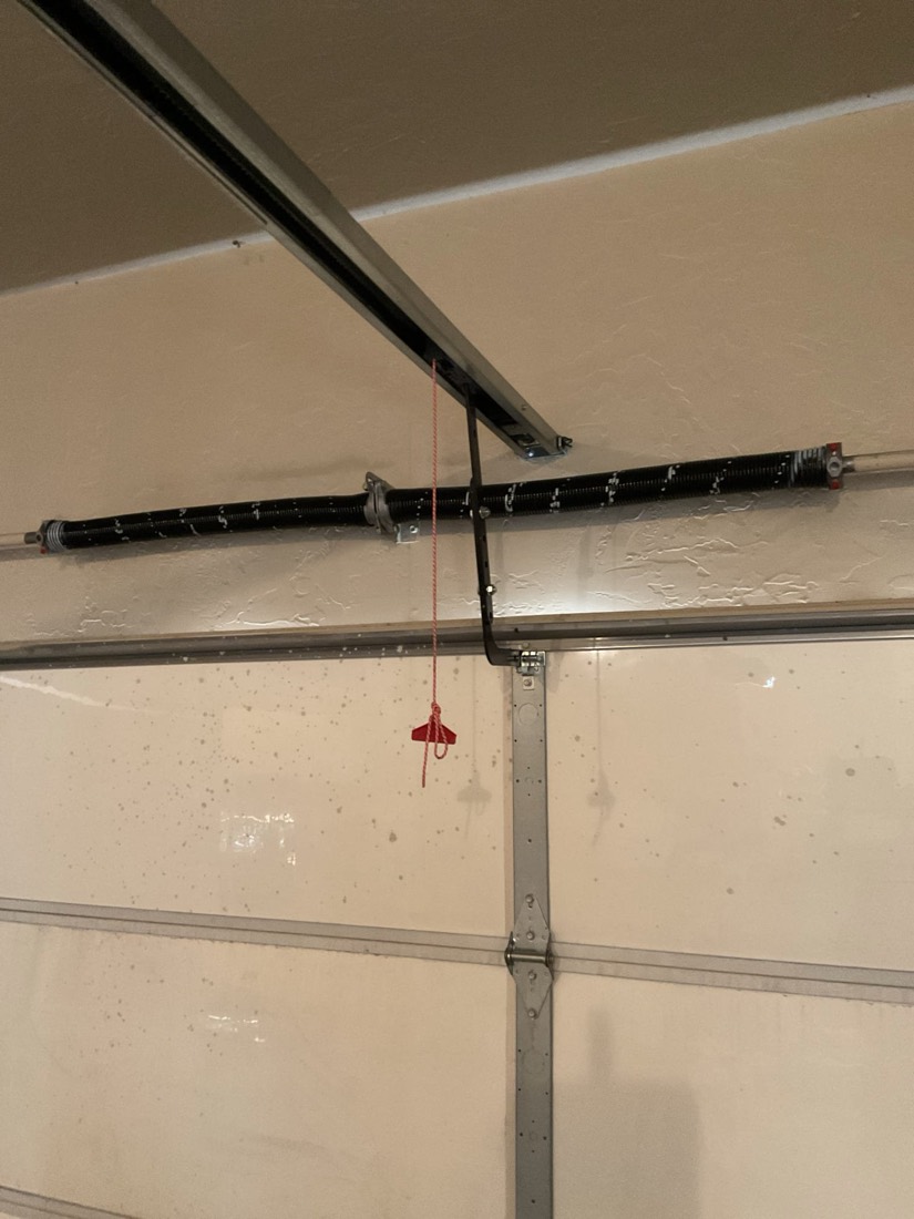New black garage door spring installed with red emergency release cable visible.