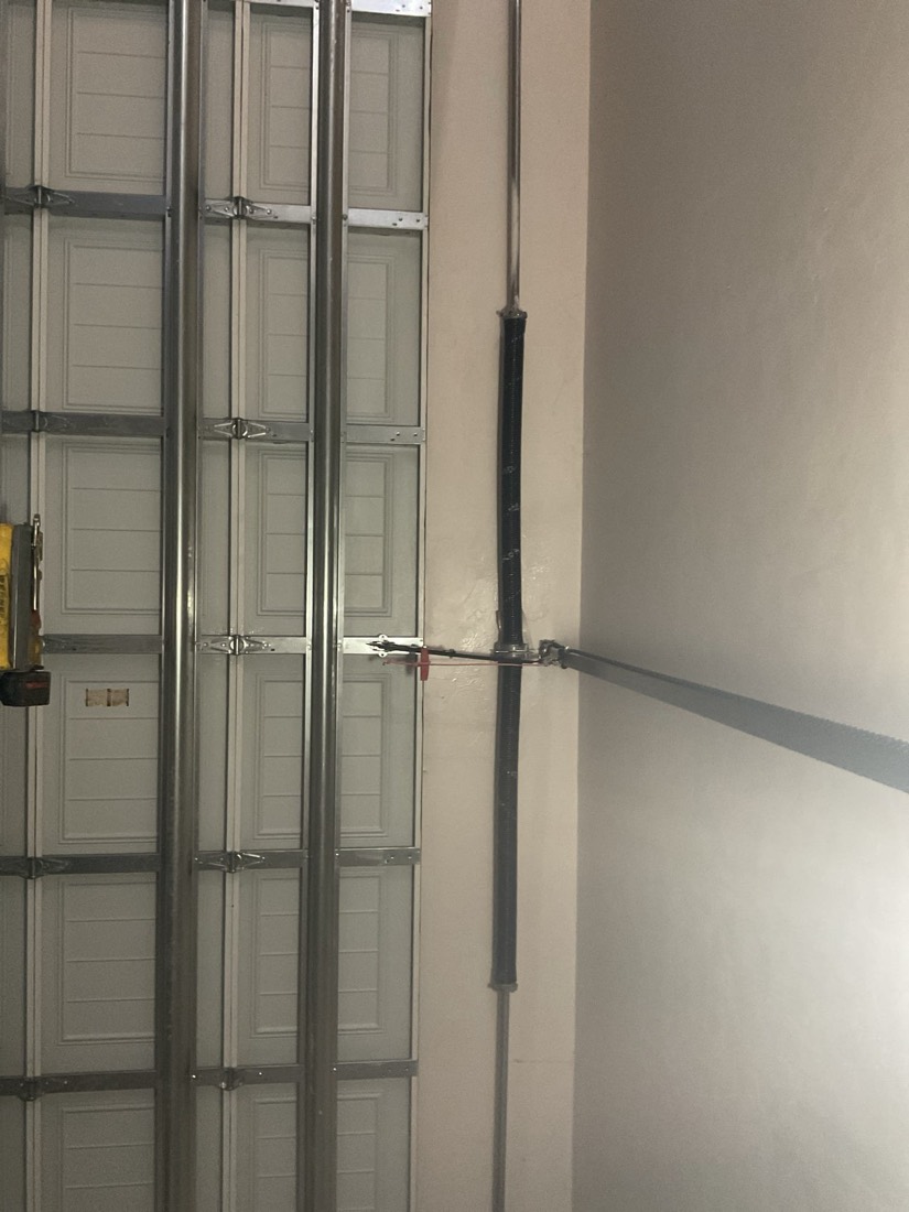 Newly installed black garage door torsion spring on a sectional garage door.