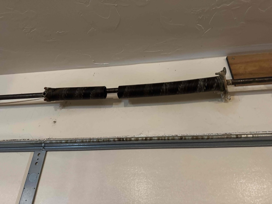 Garage door torsion springs and cable hardware mounted inside door frame.