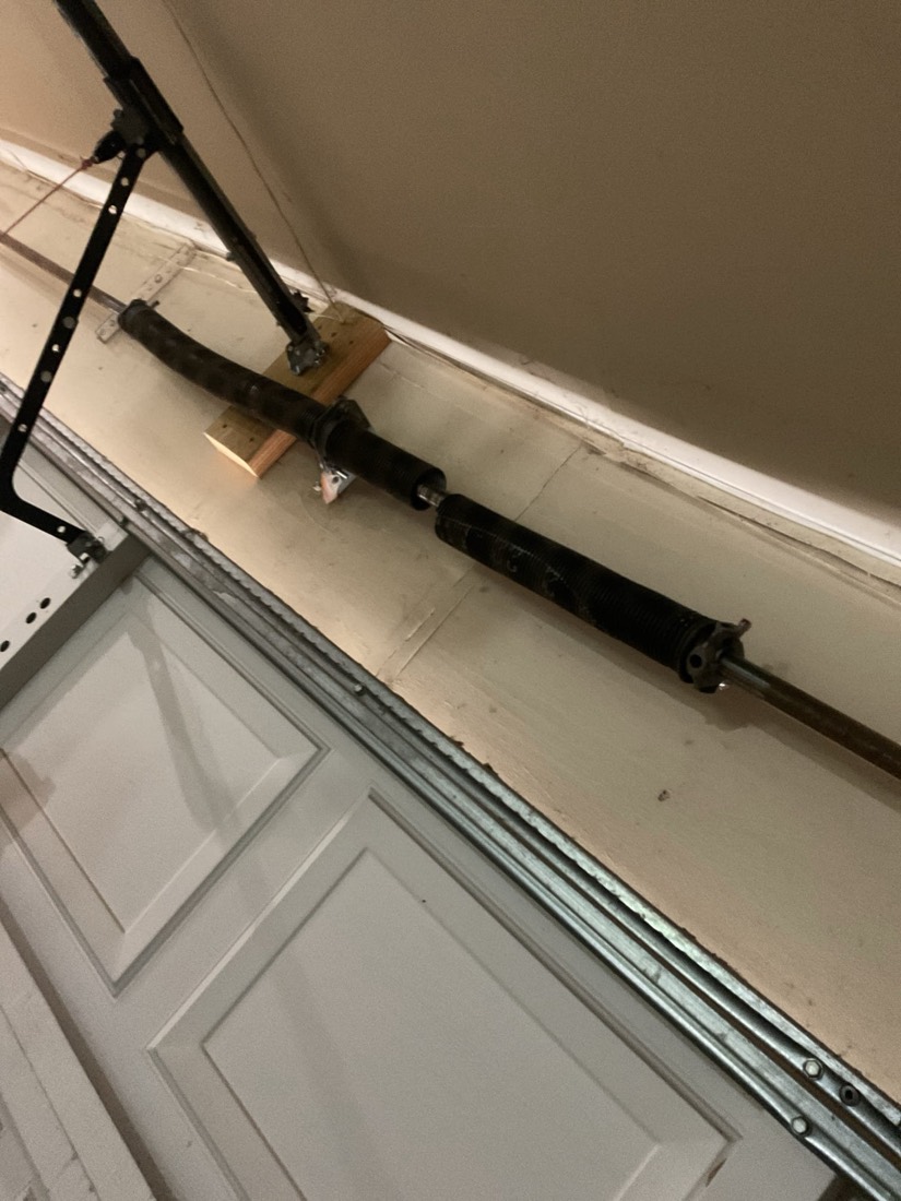 Black garage door spring and hardware mounted on garage door frame.