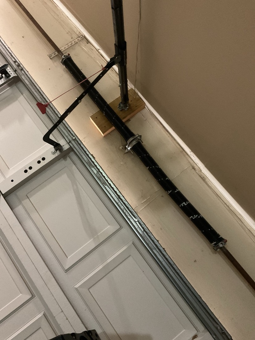 Newly installed black garage door spring with hardware on white garage door frame.