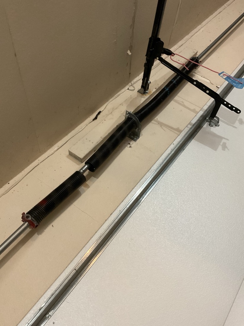 New garage door spring with safety cable installed on door frame during repair.