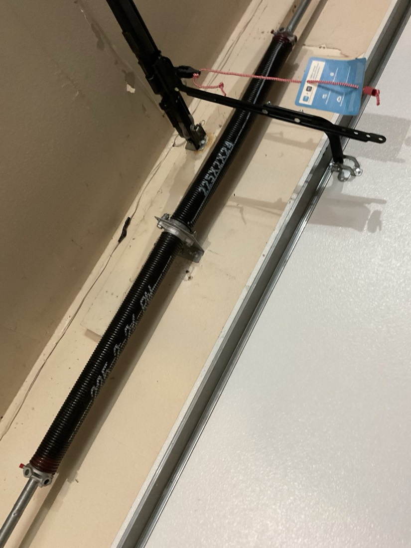 Replacement garage door spring installed in residential door frame with safety cable and hardware.
