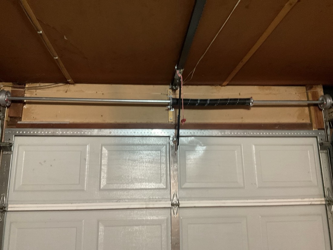 Garage door spring and hardware assembly installed on white two-panel residential door