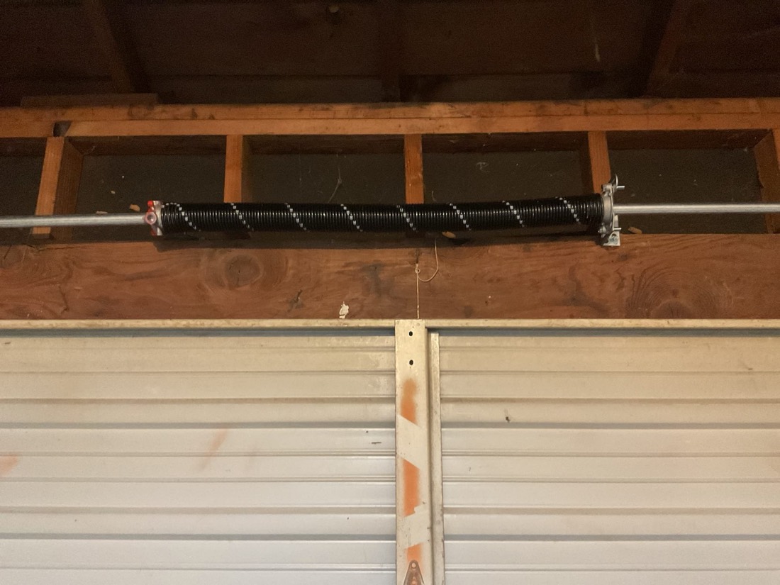 New garage door torsion spring with drum and pulley system installed in garage.