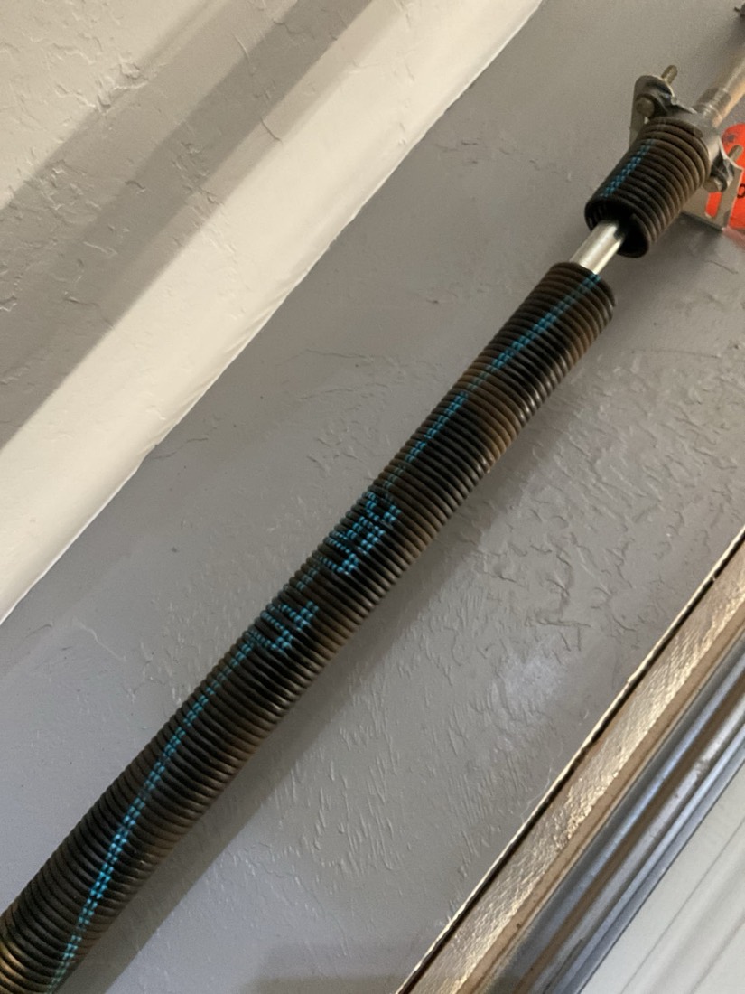 New black garage door spring with blue markings installed